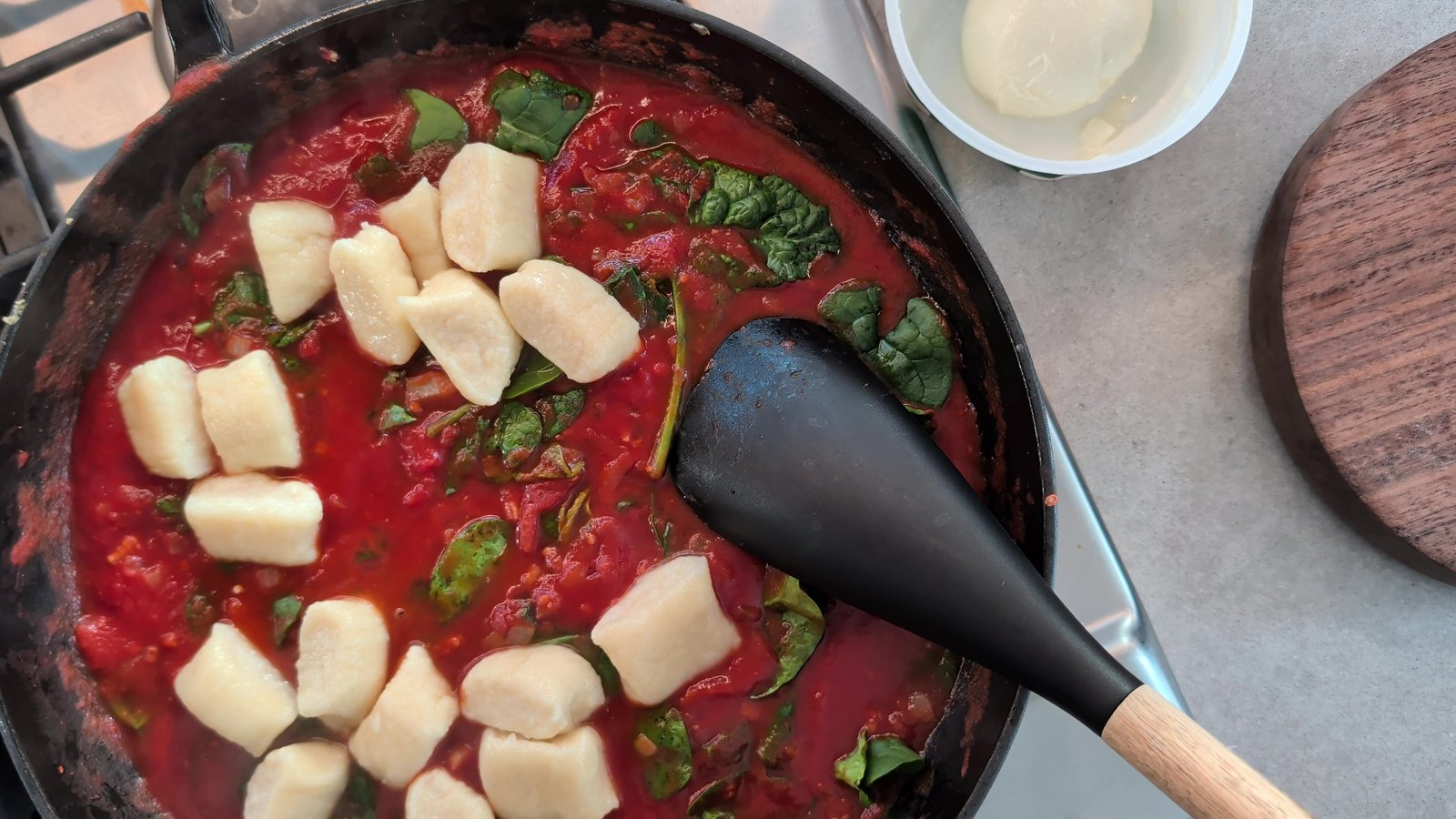 Homemade ricotta gnocchi being stirred into tomato sauce